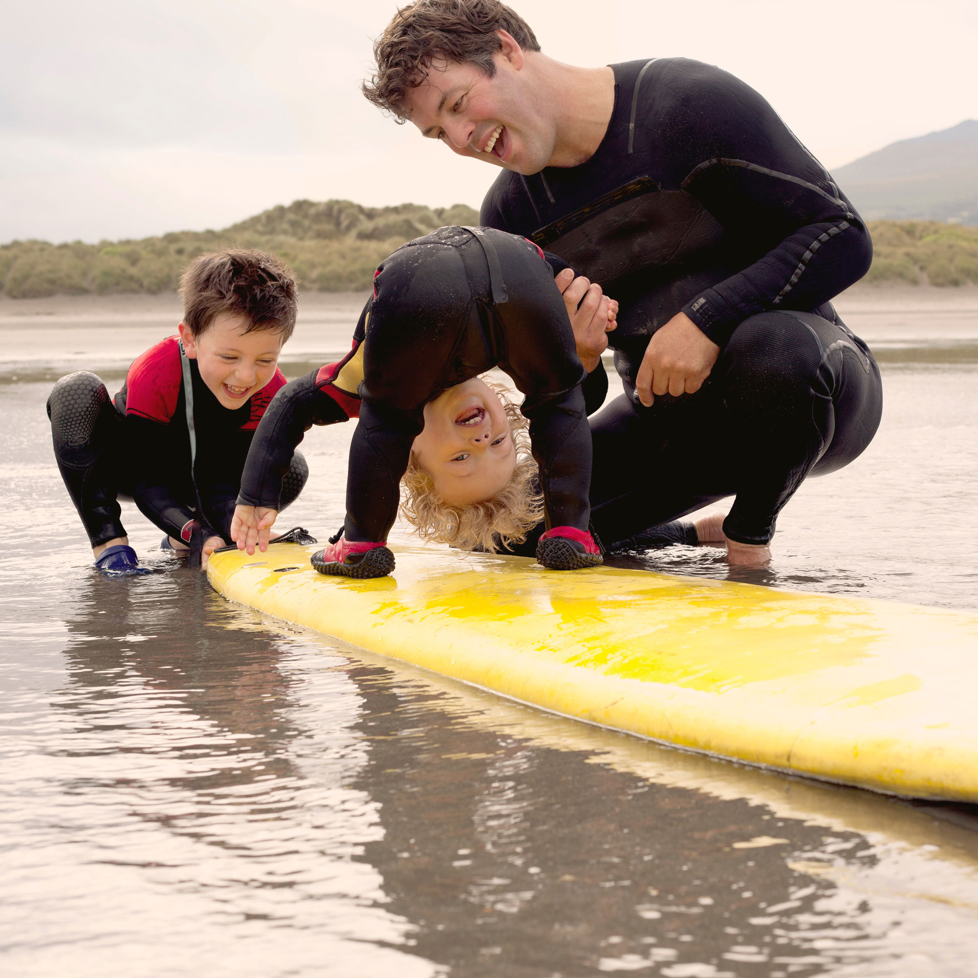 Pappa och två barn med en surfbräda i vattnet