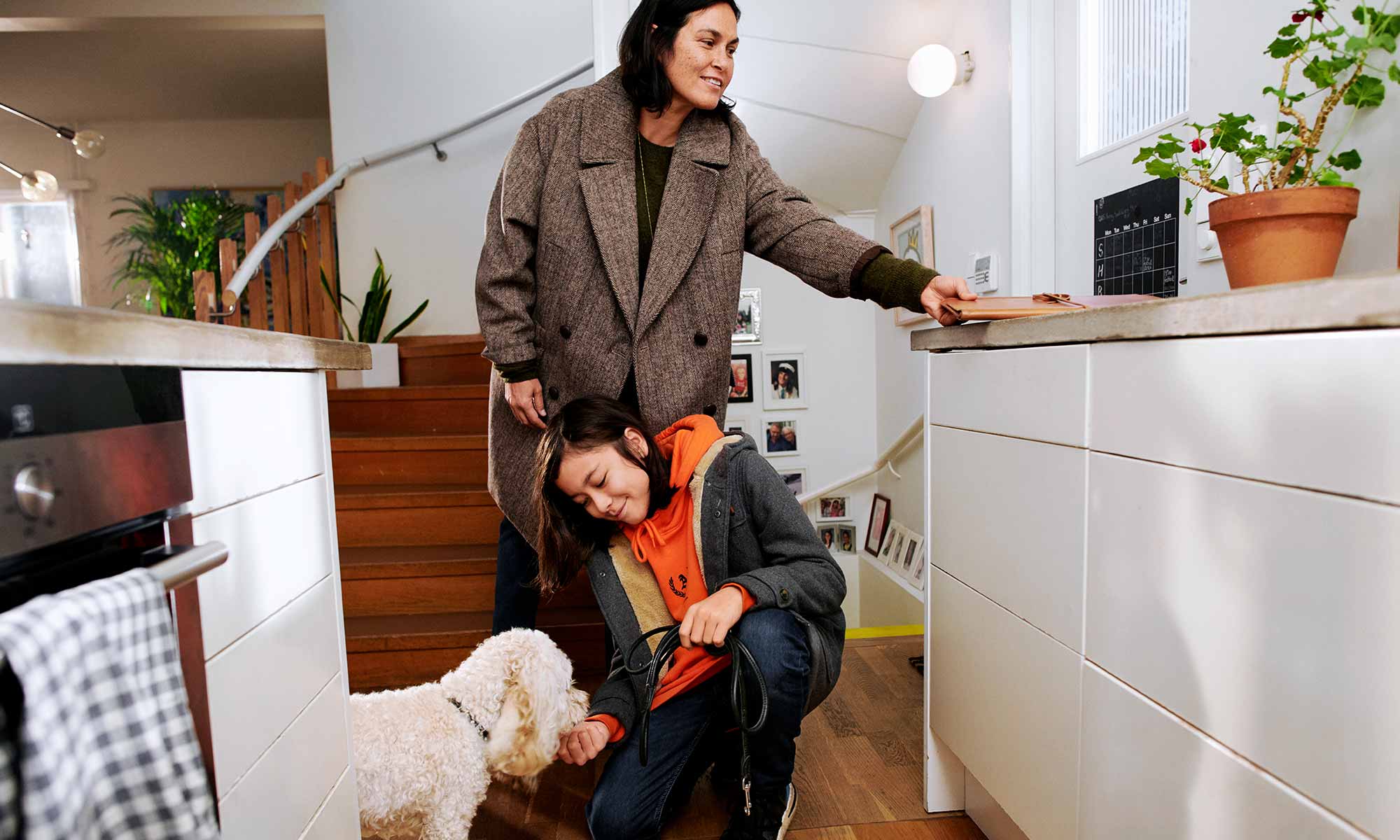 Mamma, barn och hund står i köket med jackor på