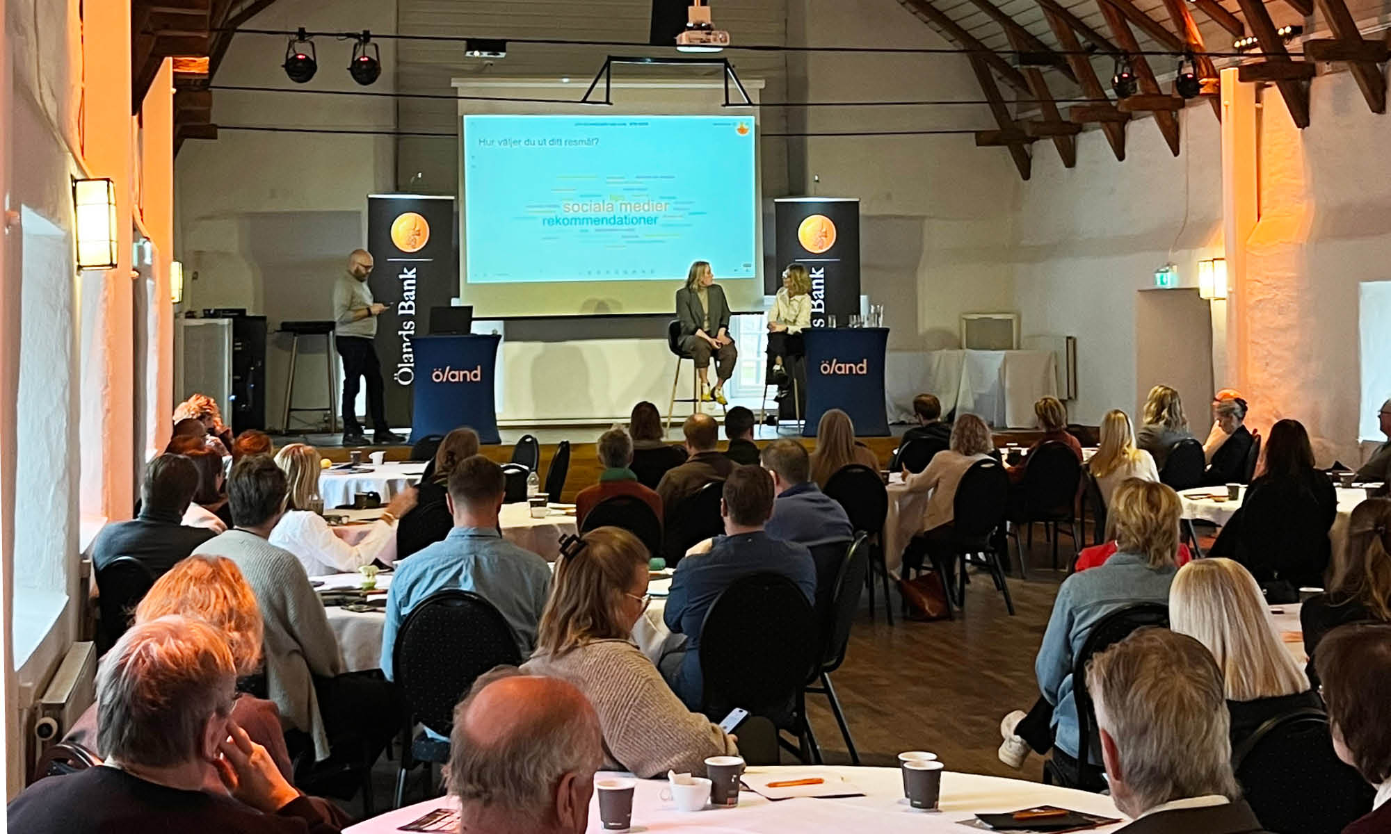 Two people on stage talking in front of audience.